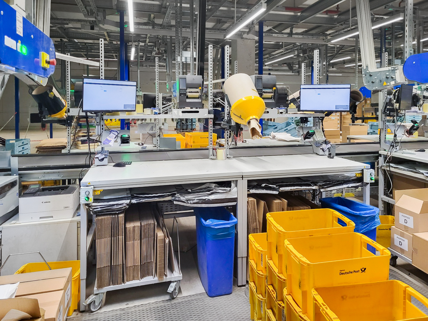 Table d'emballage ERGO-line dans le secteur logistique, équipée d'écrans, d'un scanner, d'une tablette de rangement, d'un magasin à boîtes pliantes mobile et d'étagères